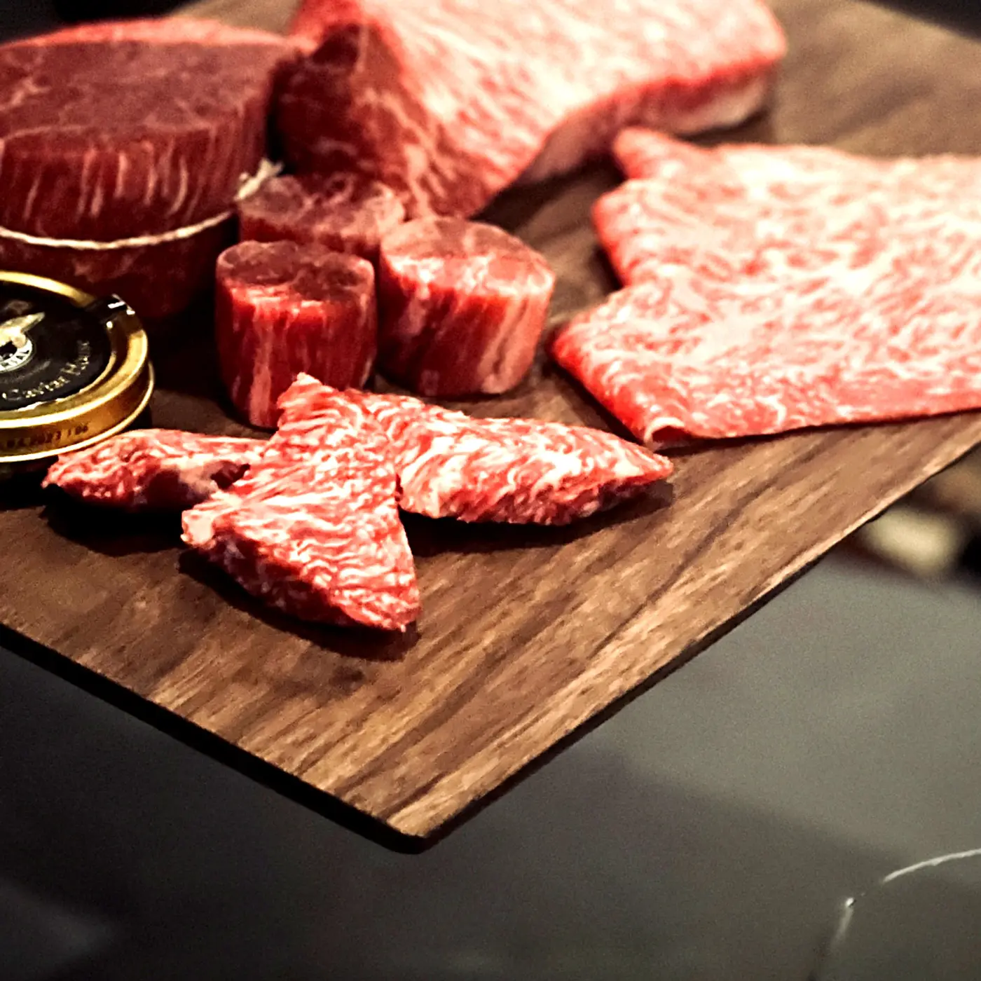 Assorted raw Hanwoo cuts with intricate marbling arranged on a walnut board beside a tin of caviar