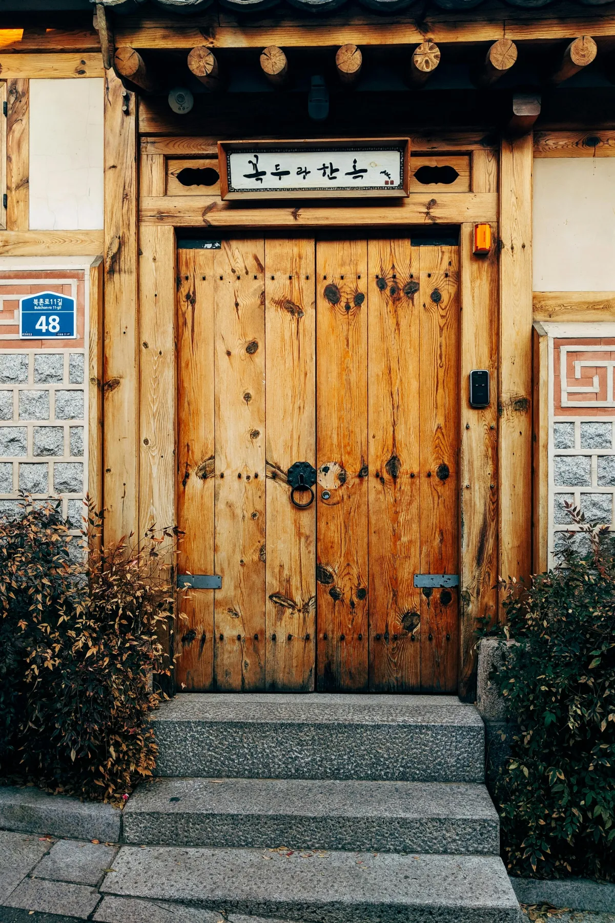 Wooden double doors of a traditional hanok on Bukchon-ro 11-gil with a hand-painted hangeul signboard above