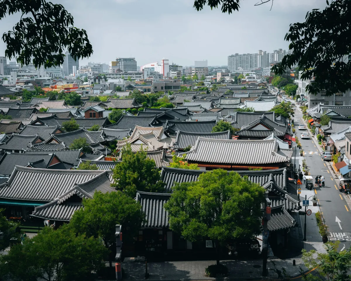 Elevated view of a traditional hanok village with sweeping tiled rooftops set against a modern Seoul skyline