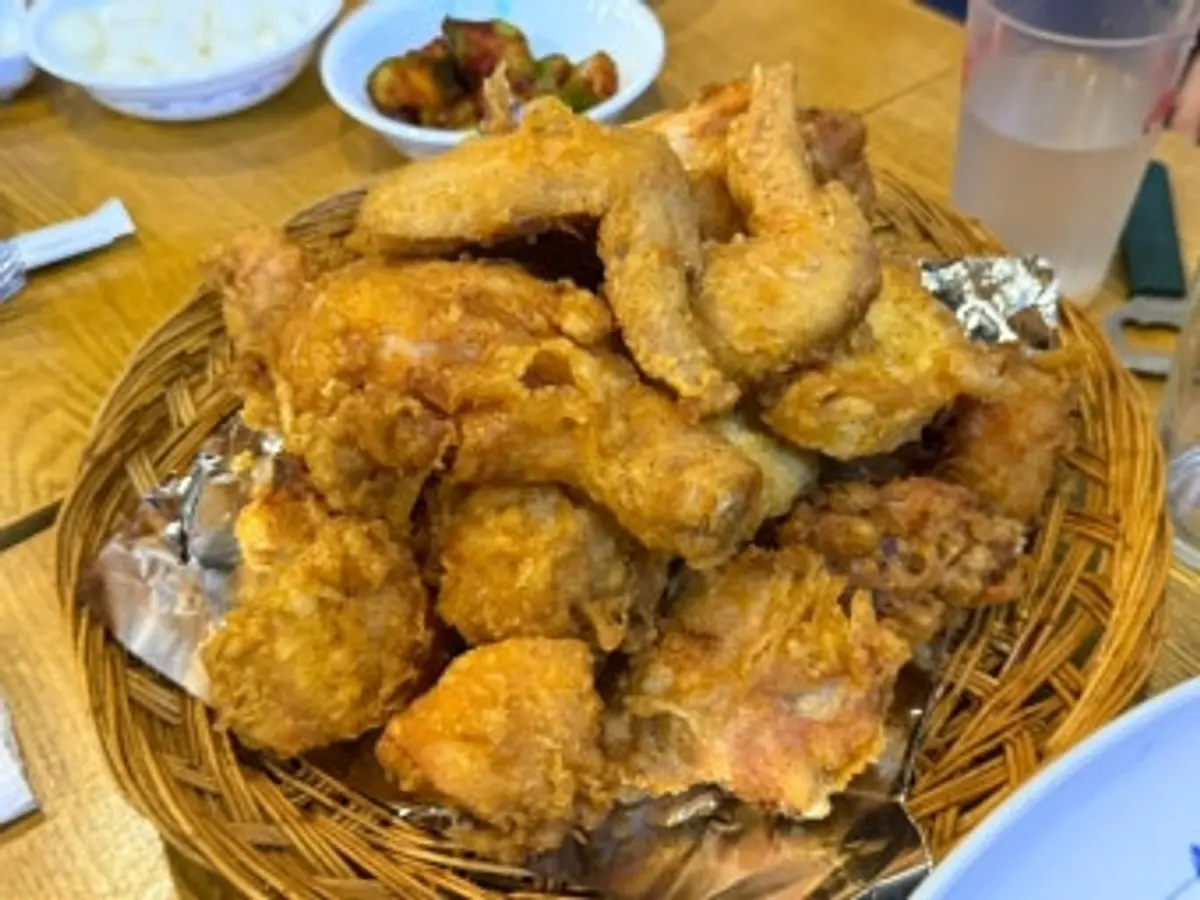 잘 짜인 대나무 바구니에 수북이 담긴 황금빛 한국식 프라이드치킨과 옆에 곁들여진 단무지 반찬