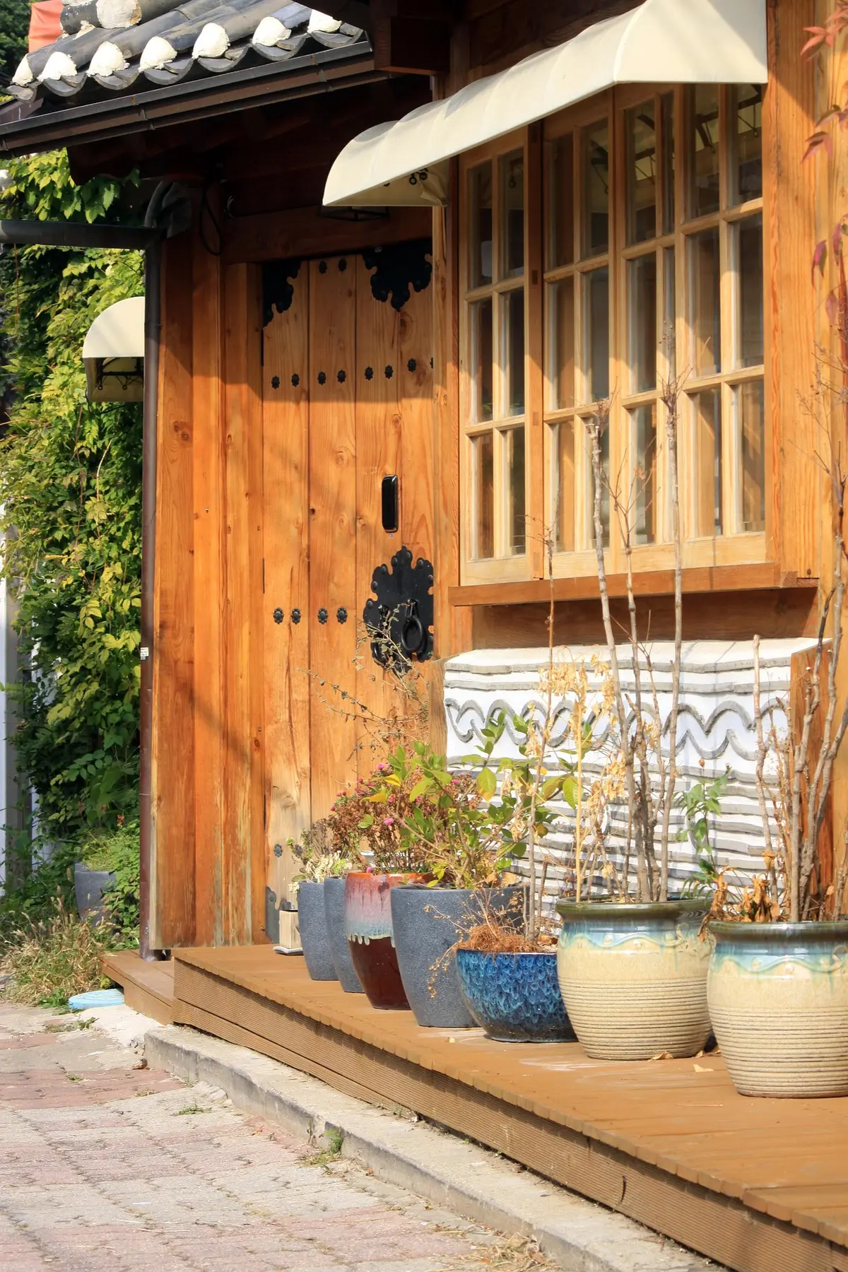 Wooden hanok entrance with iron door knocker and ceramic planters lining a sunlit porch in Bukchon
