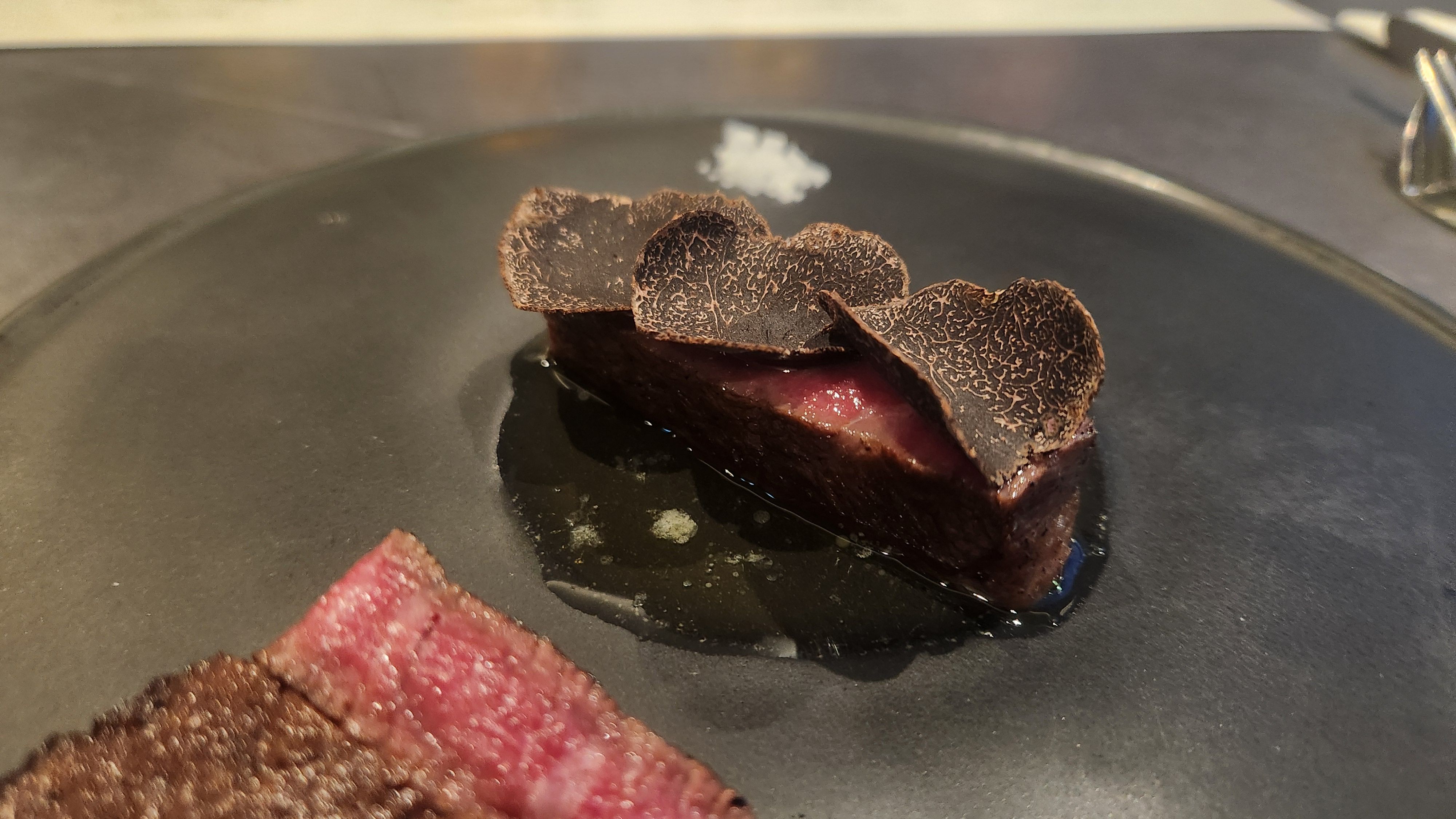 Seared Hanwoo beef crowned with shaved black truffle, served with sea salt on a dark ceramic plate