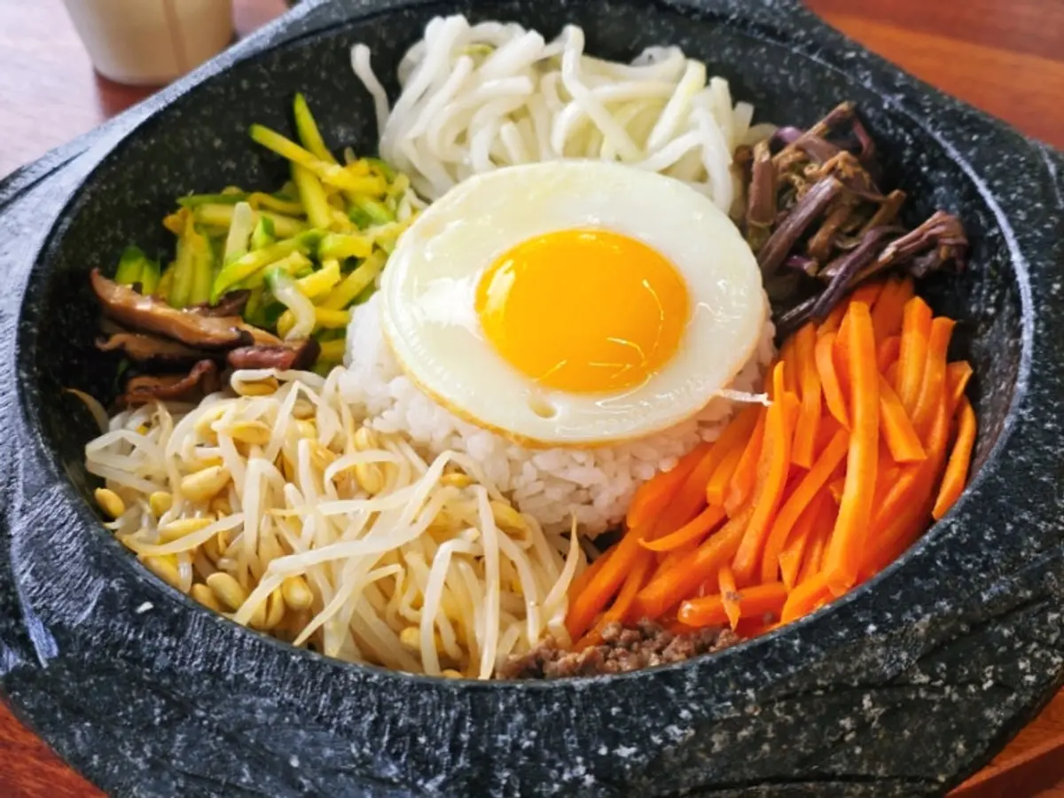 반숙 달걀, 콩나물, 당근, 고사리, 소고기가 올라간 뜨거운 돌솥의 돌솥비빔밥