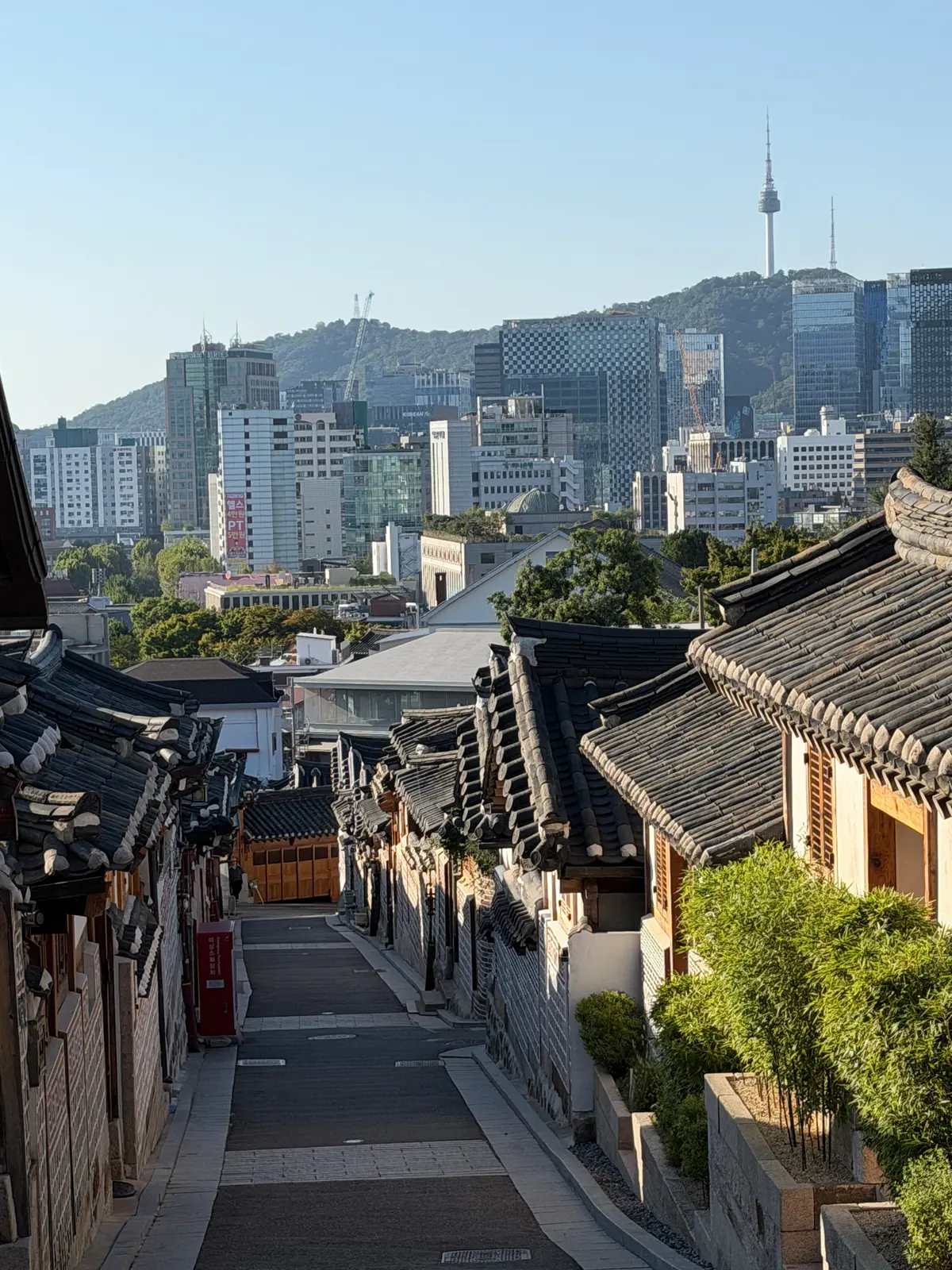 A hanok alley in Bukchon sloping downhill toward the Seoul skyline and N Seoul Tower