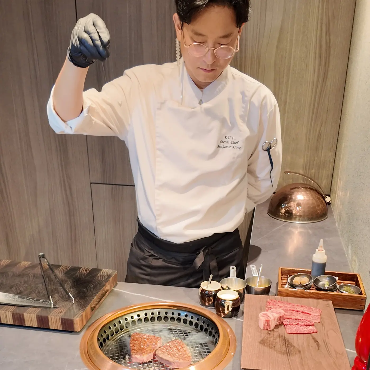 오마카세 카운터의 구리 그릴 위에서 한우 부위에 소금을 뿌리고 있는 KUT SEOUL 오너 셰프 벤자민 강