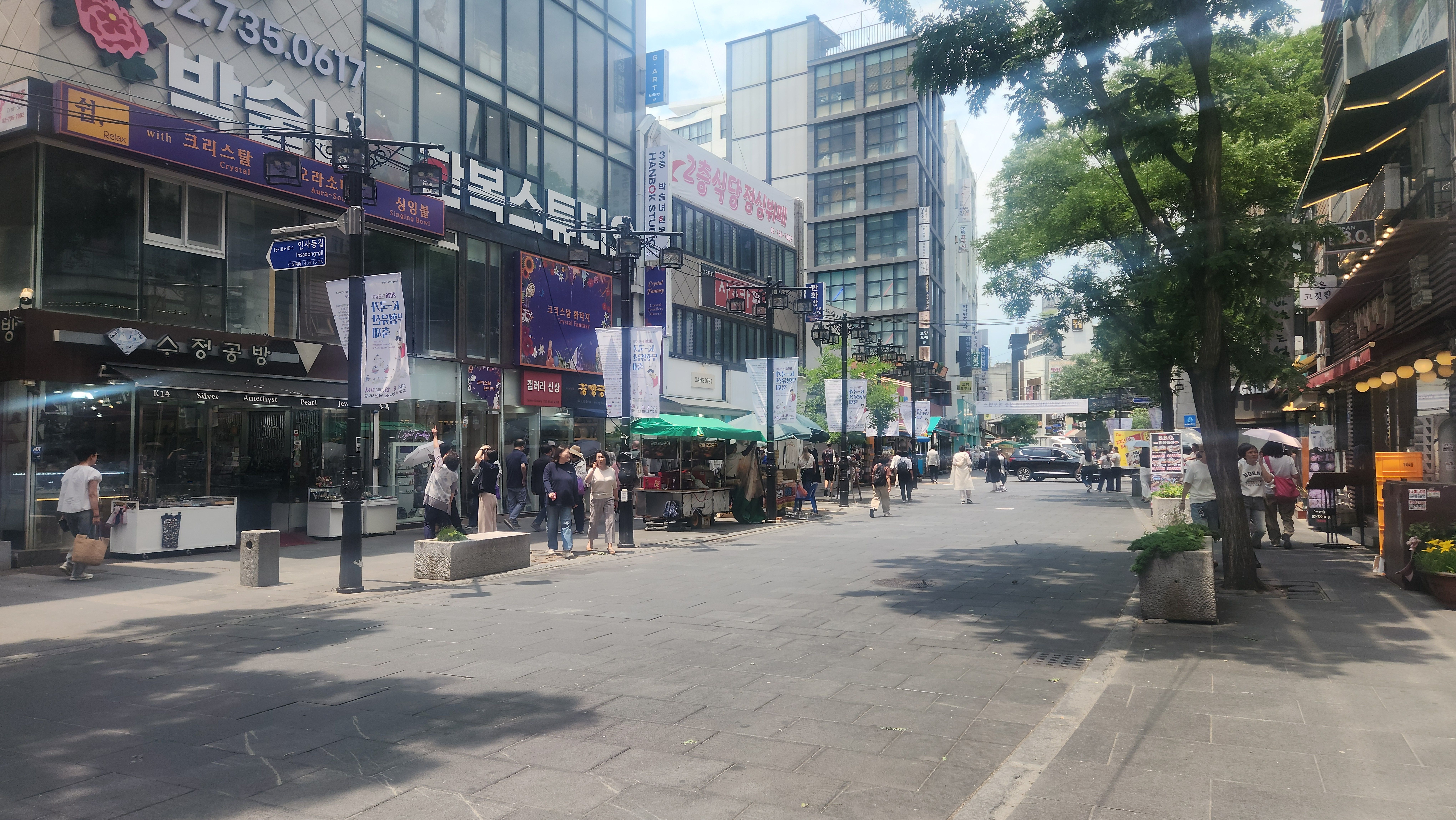 한낮의 햇살 아래 한복 스튜디오, 공예품 가게, 여름 산책객들로 늘어선 종로 인사동길 보행자 거리
