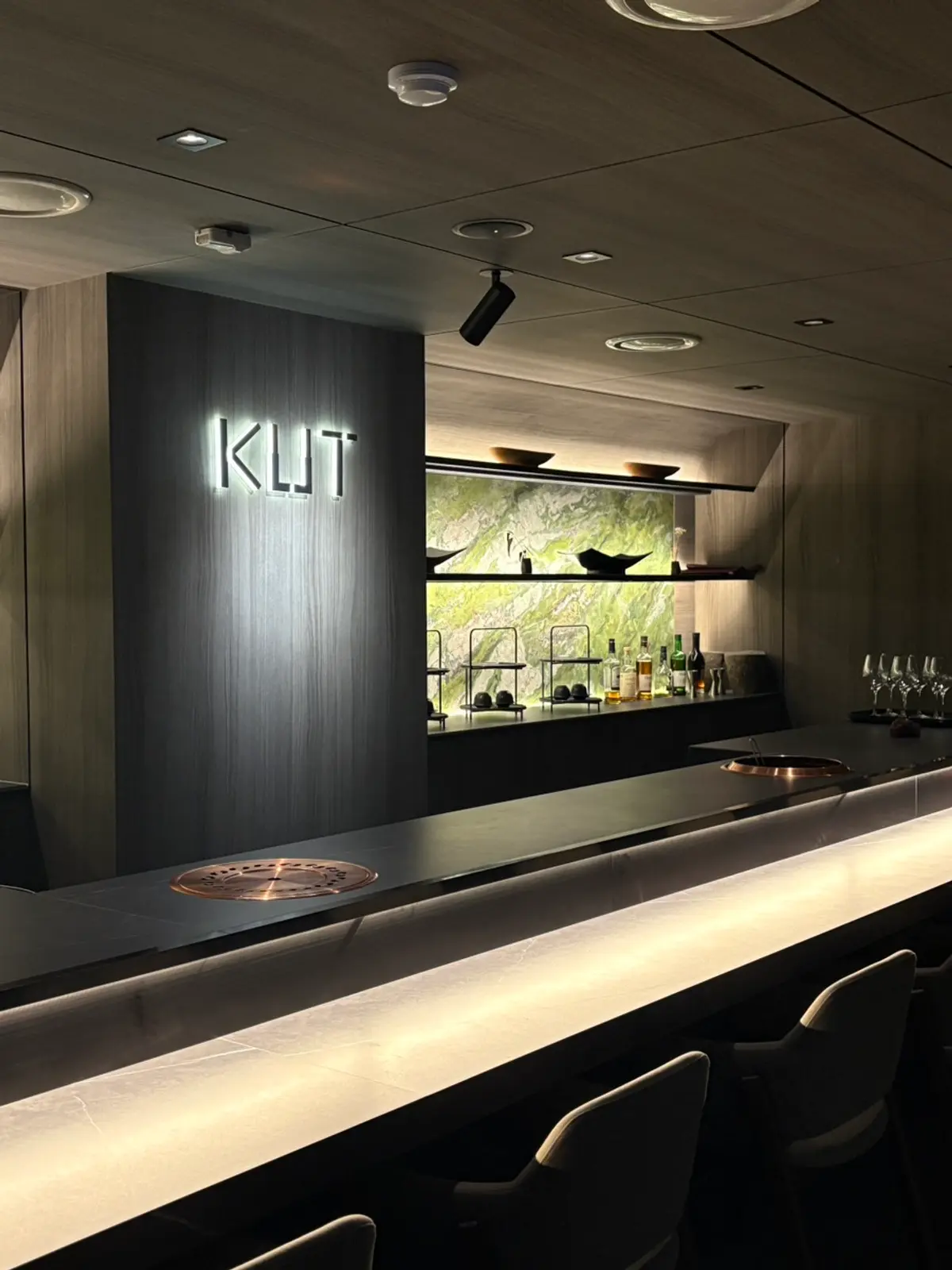 KUT Seoul Omakase吧台，灯光招牌、铜制烤盘、绿色大理石层架与精选威士忌陈列