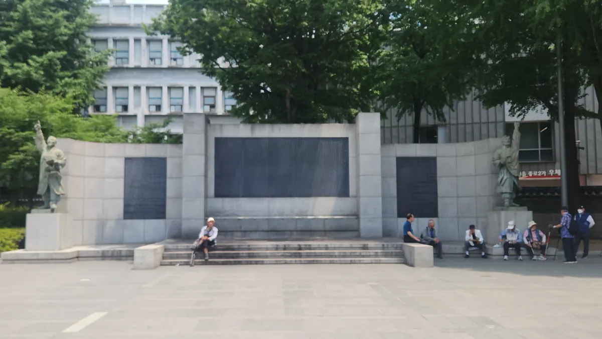 여름 나무 아래 돌계단에서 쉬는 어르신들과 함께 자리한 종로 탑골공원의 3·1 독립운동 기념물