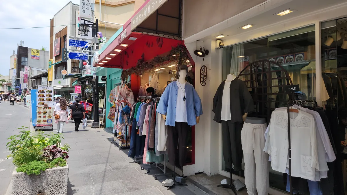 陽光降り注ぐ通り沿い、マネキンに掛けられた現代的な韓服風リネン衣装を展示する仁寺洞のブティック店頭