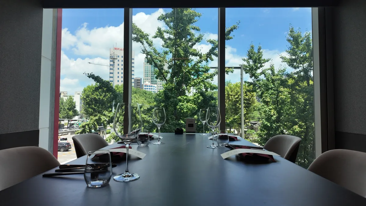 Private dining room at KUT Seoul with wine glasses set against a floor-to-ceiling window framing Jongno ginkgo trees