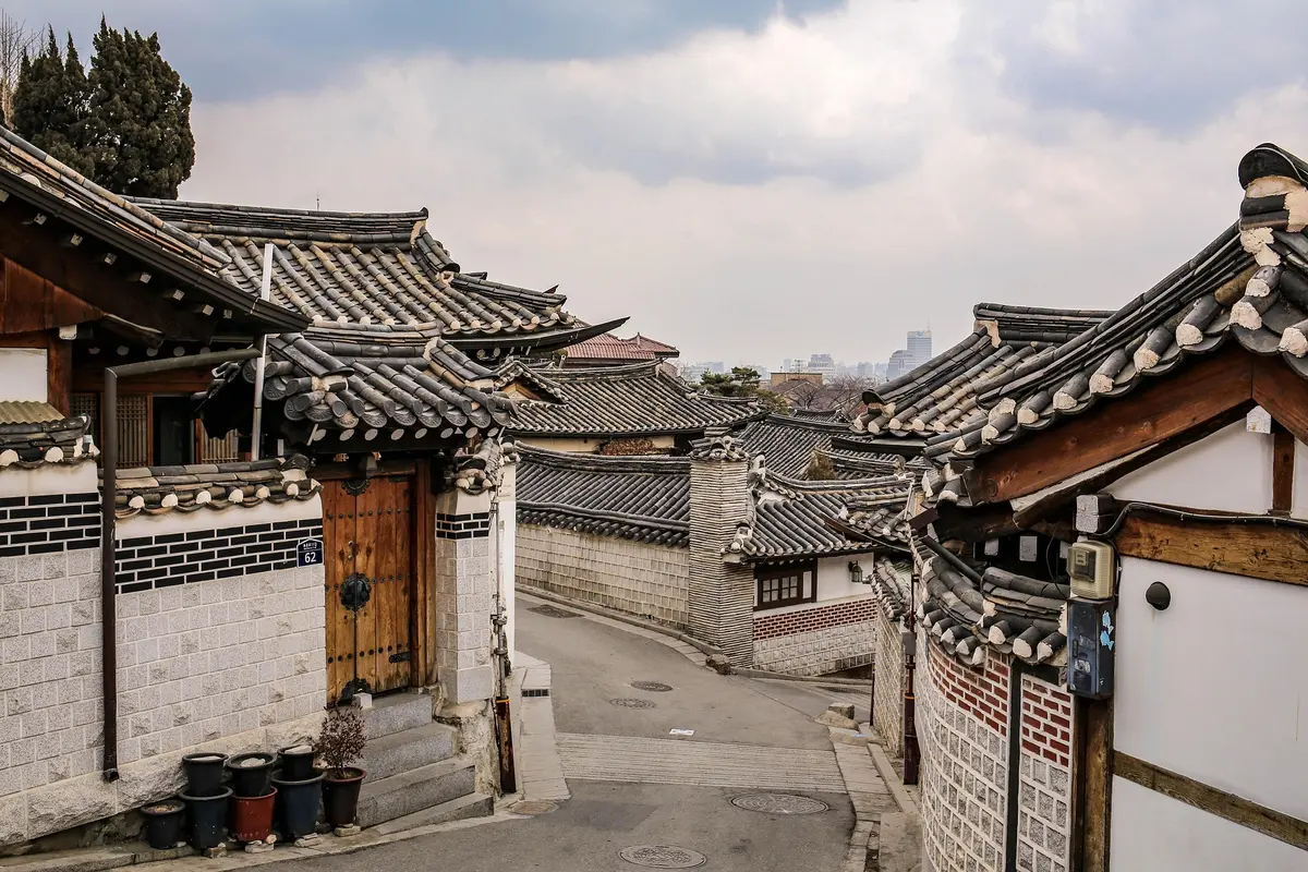 Tiled hanok rooftops and quiet alleyway of Bukchon Hanok Village with Seoul skyline rising in the distance
