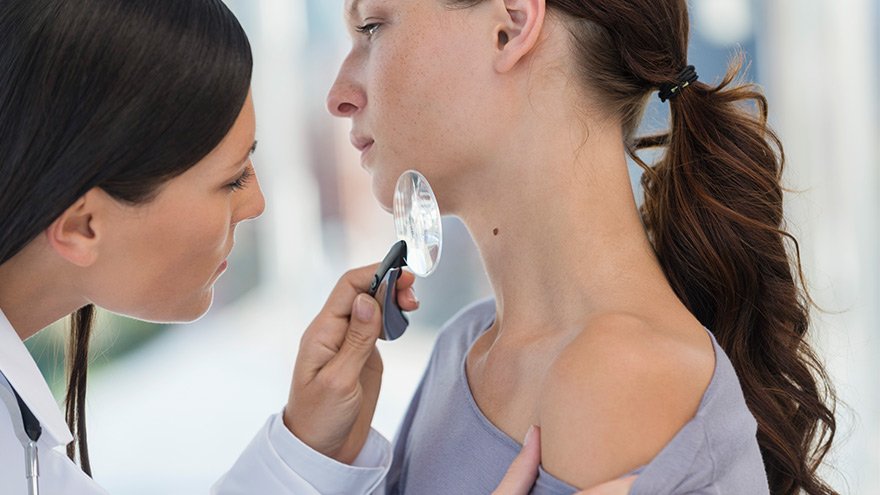 Dermatologist using magnifying glass to examine woman's skin