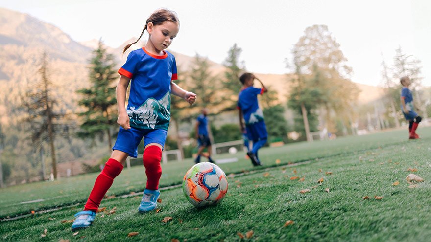 Young girl soccer player exercises with a ball while running on the soccer field