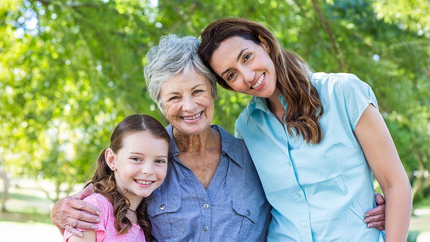 A woman with her mom and her daughter, hugging and smiling at the camera