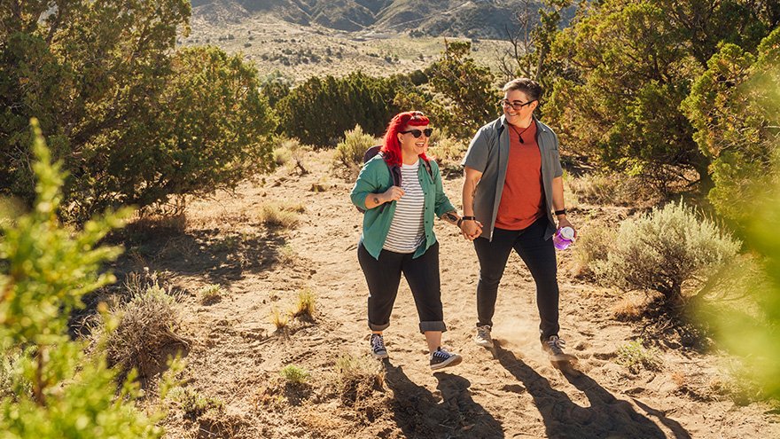 a couple are walking down a dirt path holding hands.