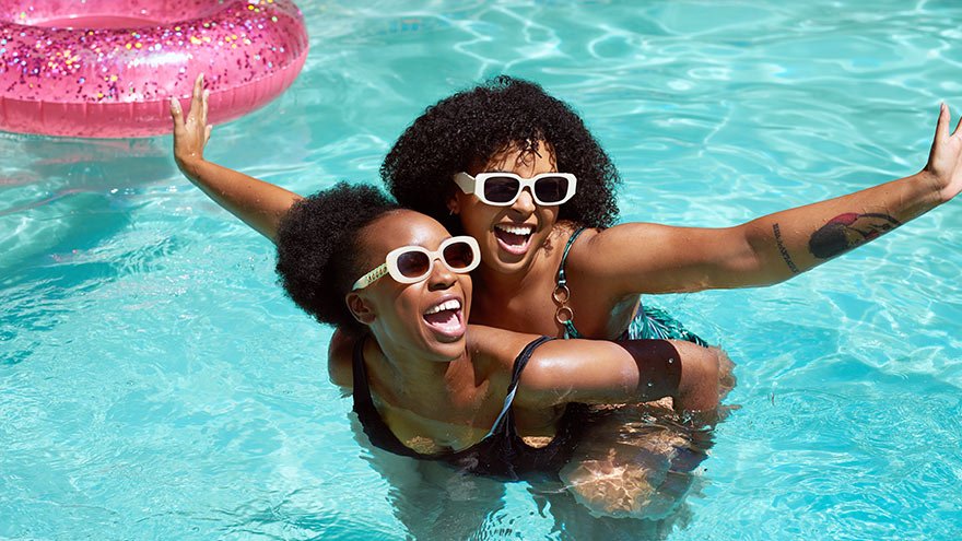 Friends having fun in the pool, piggyback swimming and laughing
