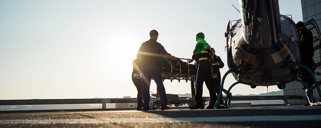 Medical team transporting patient on rooftop of hospital next to helicopter