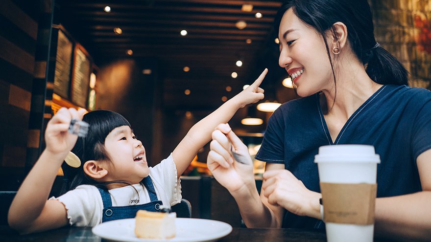 Young Asian mother and little daughter sharing a slice of cheese cake in cafe