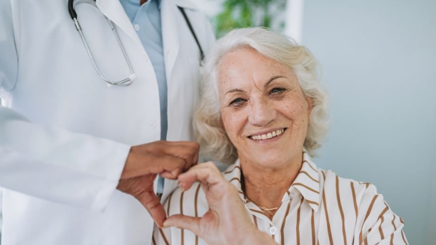An elderly female patient smiles with her cardiologist and signals a heart with her hands