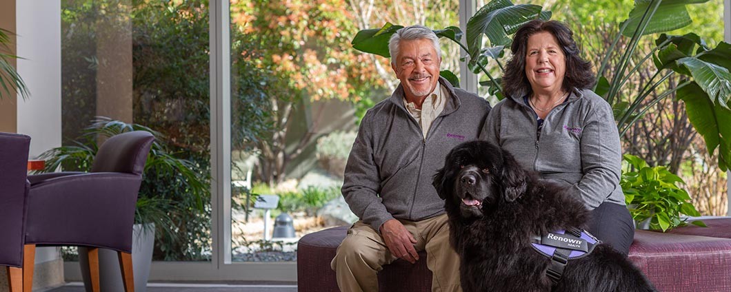 Two Renown Health volunteers sitting with a therapy dog.