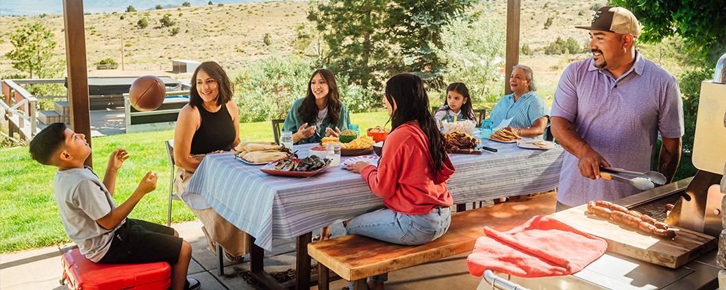 a family is sitting at a table on a porch eating food .