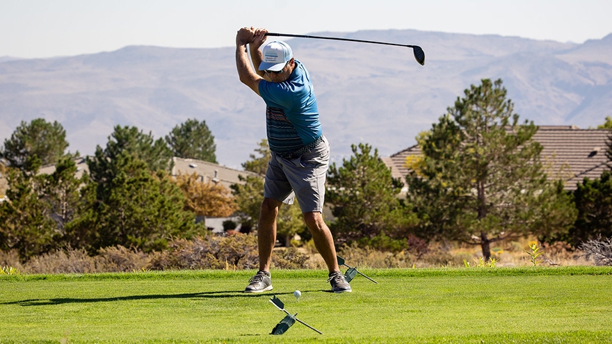Participant swinging at golf ball in the Cancer Classic at ArrowCreek.