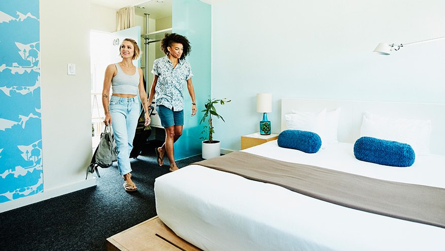 Smiling couple walking into hotel room carrying luggage