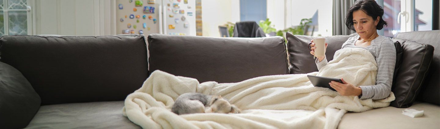 Woman at home, sick with puppy laying near, checking symptoms on iPad