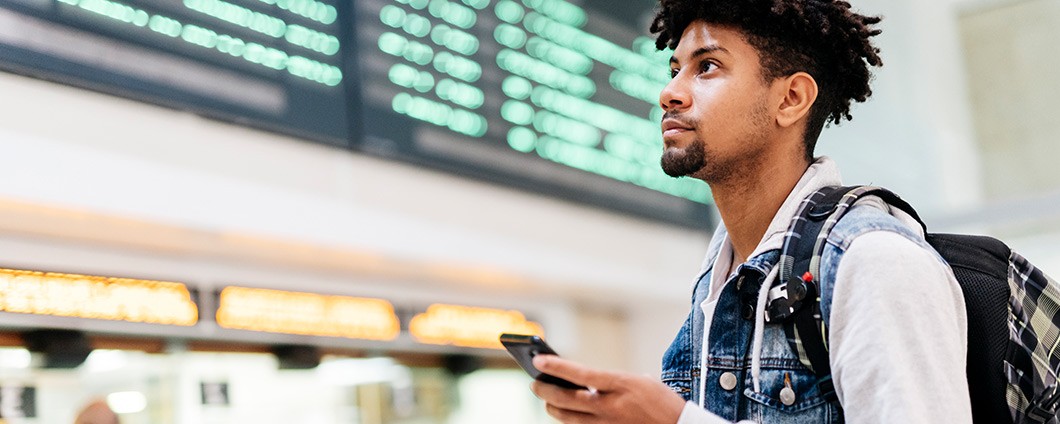 Young man at the airport looking at the list of destinations holding a cell phone