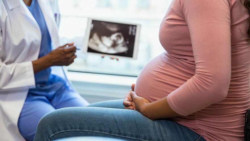 Provider explaining baby health with expectant mother, baby monitor displayed in background