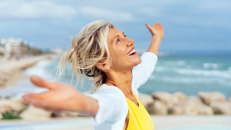 Joyful woman enjoying the freedom of the beach standing with open arms and a happy smile looking up towards the sky