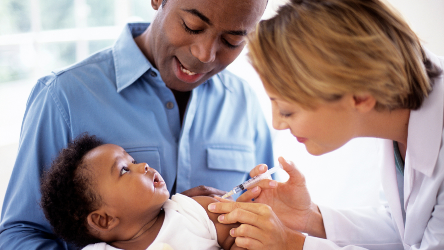 A parent holds a young baby as a doctor prepares to immunize