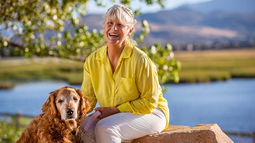 Women smiling and sitting with her dog by a pond