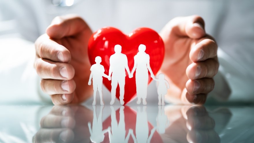 A doctor's hands cup a red heart with an outline of a family holding hands in front of it.