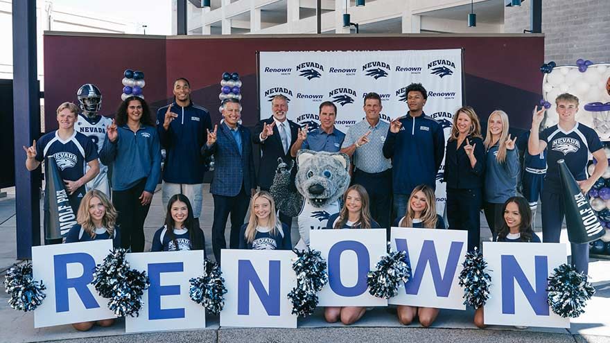 Renown Health and University of Nevada leaders, student-athletes, cheerleaders and the Wolf Pack mascot pose in front of a Renown and Nevada step-and-repeat banner, holding letters spelling RENOWN.
