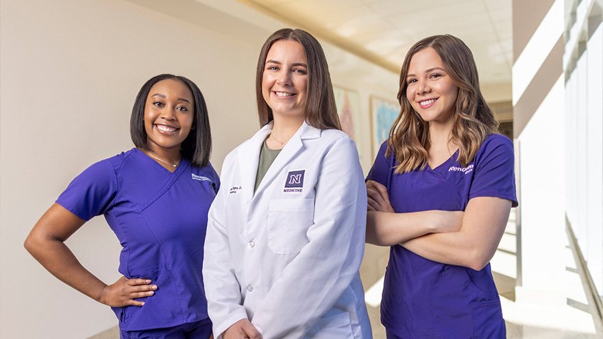 three female nurses are posing for a picture in a hospital hallway .