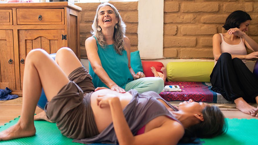 Beautiful mature doula with natural grey hair examines a pregnant woman