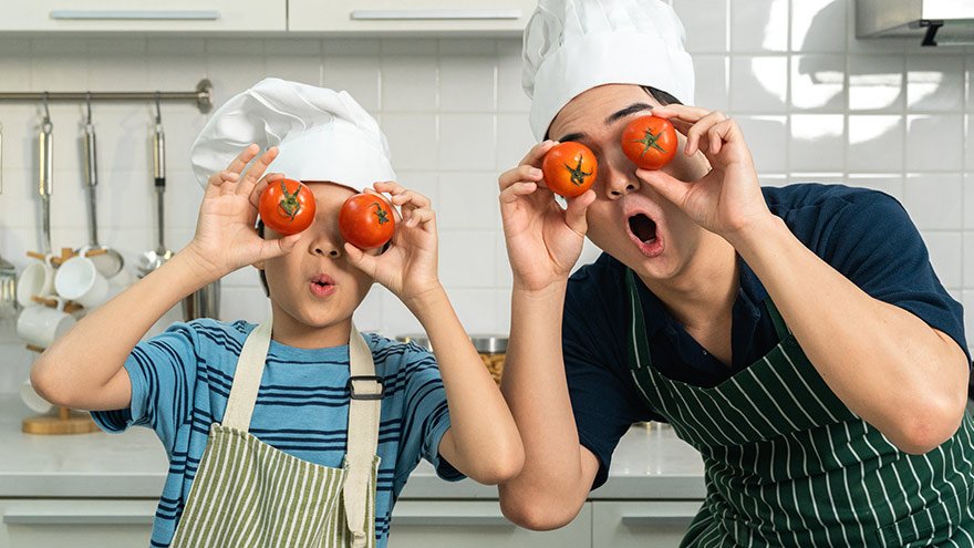 Asian father and son cooking in the kitchen holding tomatoes over their eyes