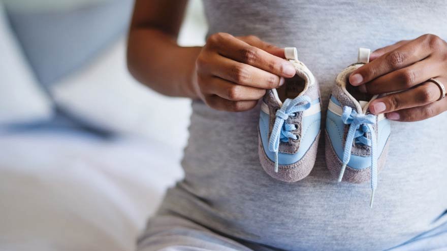 Expecting mom holding baby shoes against her belly