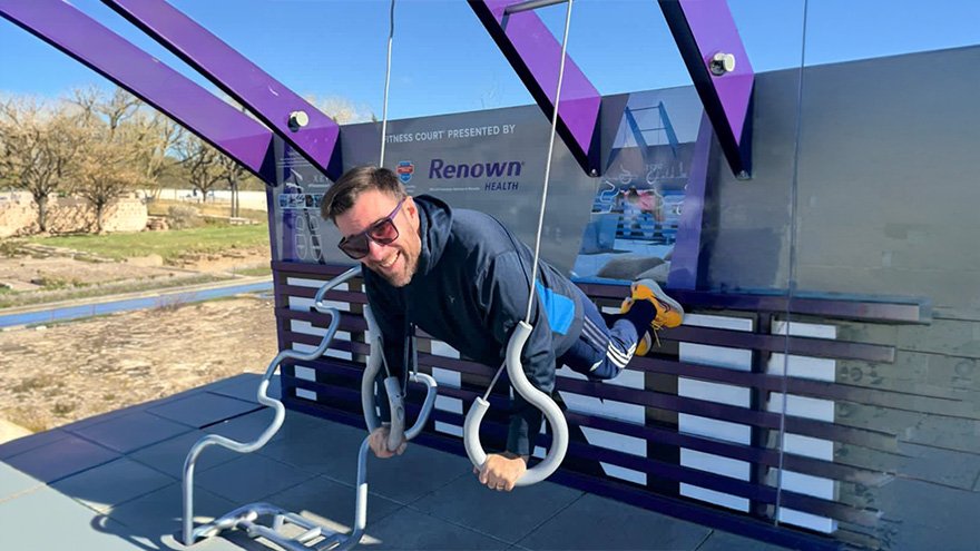 Dr. Cucalon Calderon exercising with gymnastics rings on outdoor equipment.