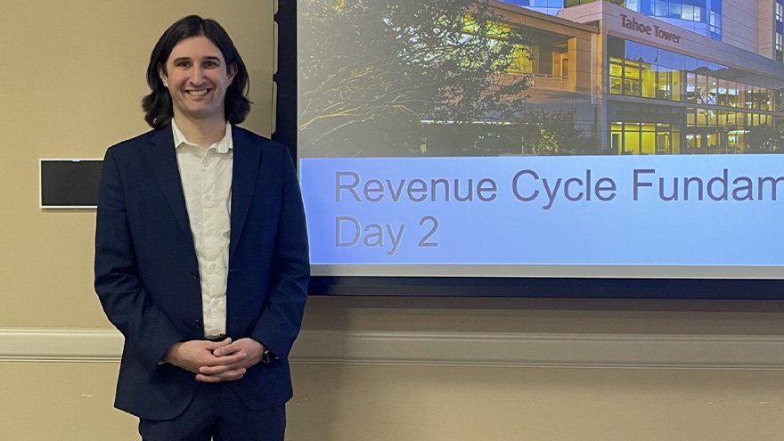 Logan, revenue cycle trainer, posing in front of presentation screen.