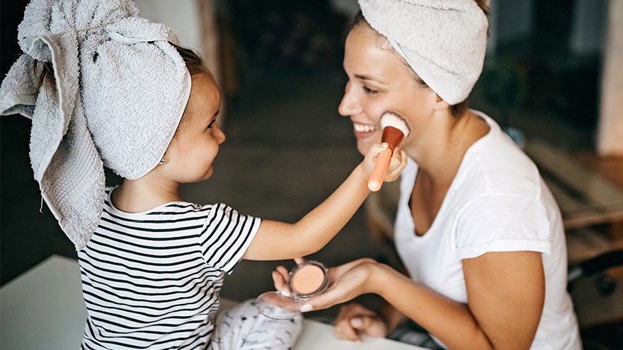 Child applying face powder with makeup brush to her mother at home