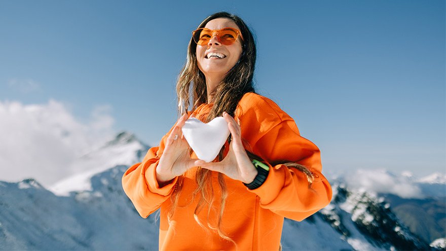 Joyful woman holding snow heart in mountain landscape