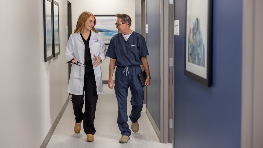 Acting physician and apprentice walking down a hallway.