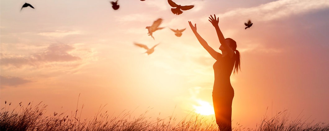Woman holding hands up to sky while doves fly in background