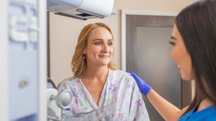 Women in patient gown stands near mammogram machine with Renown team member at her side