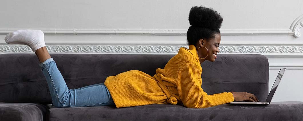 Smiling woman laying on couch typing on laptop