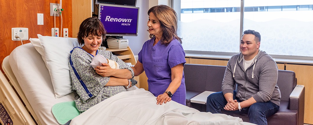 Renown OBGYN Doctor supporting female patient holding newborn baby while father looks on