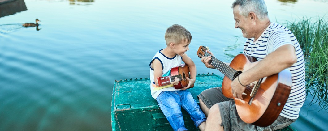 Grandfather and grandson playing guitar by lake