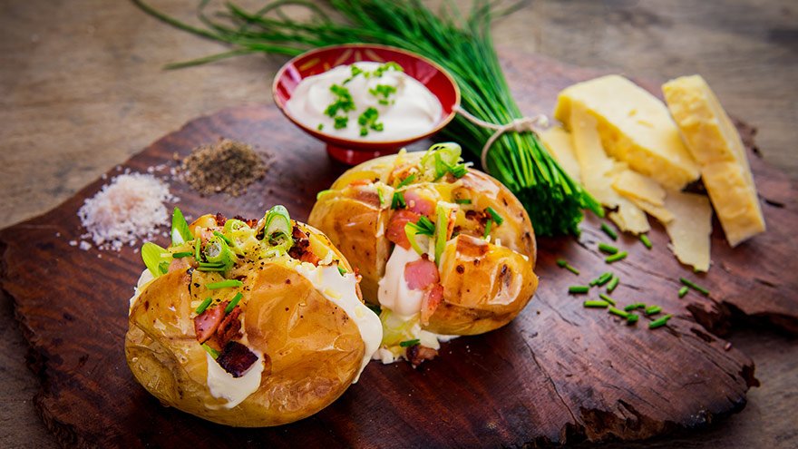 Rustic steaming hot baked potatoes topped with bacon, green onions, cheddar cheese and sour cream.